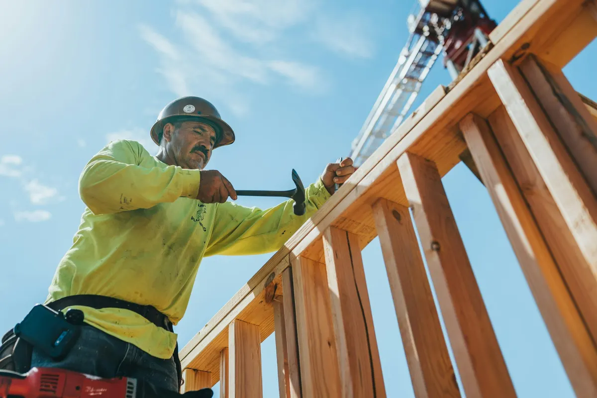 Contractor in a hard hat hammering a wooden frame on a sunny job site