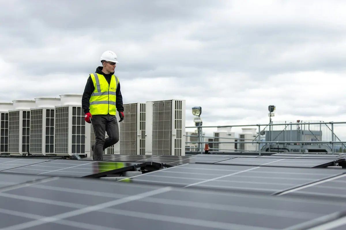 HVAC technician walking a rooftop between rows of condenser units